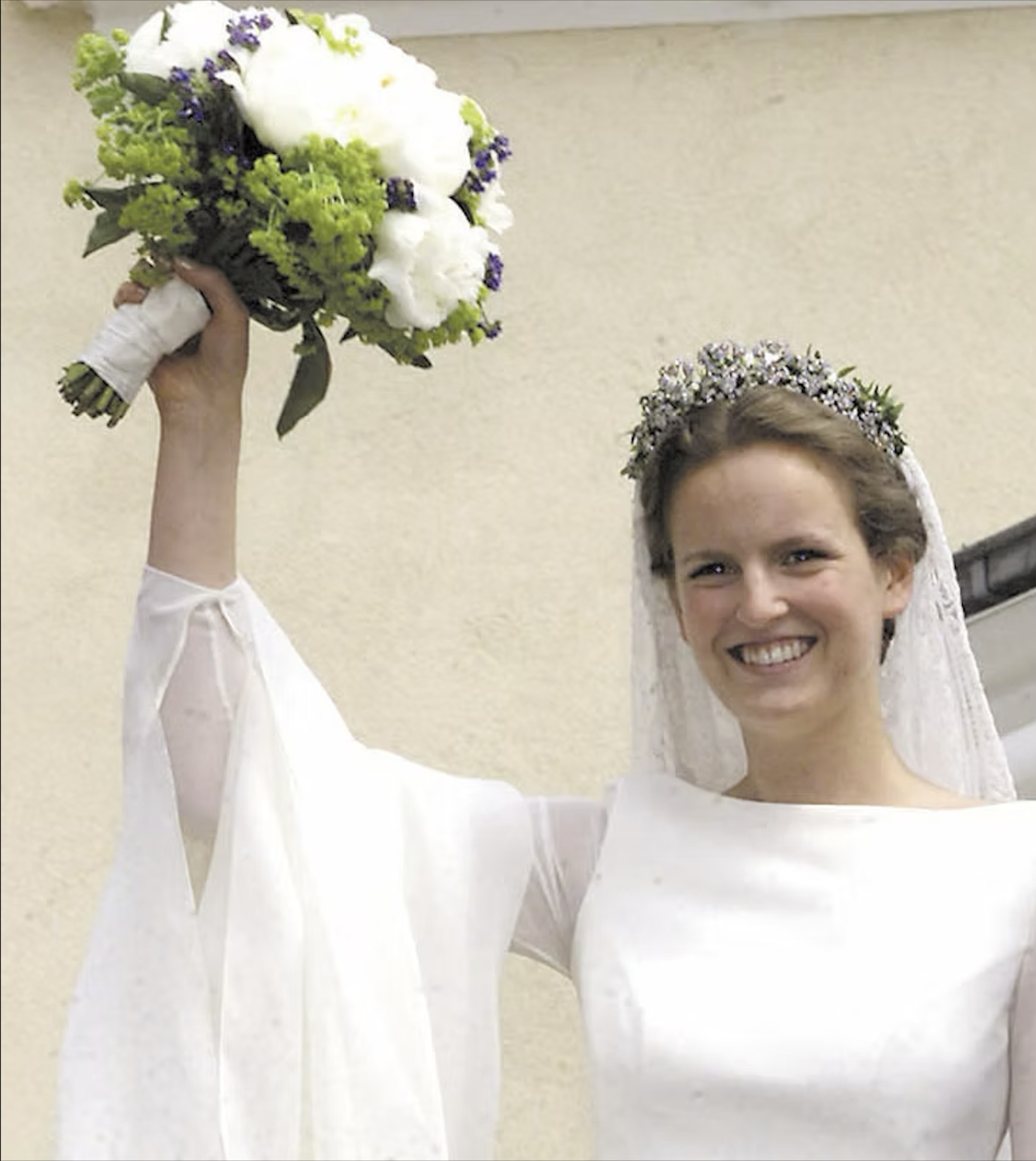Junge Frau mit Brautstrauß und Blumenkranz auf dem Kopf, lächelnd bei einer Hochzeit.