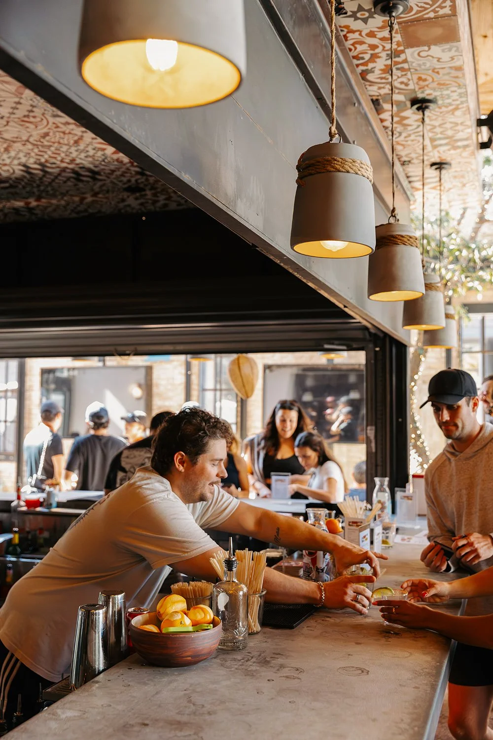 People ordering drinks at a busy bar or cafe, with hangover style pendant lights hanging from the ceiling.