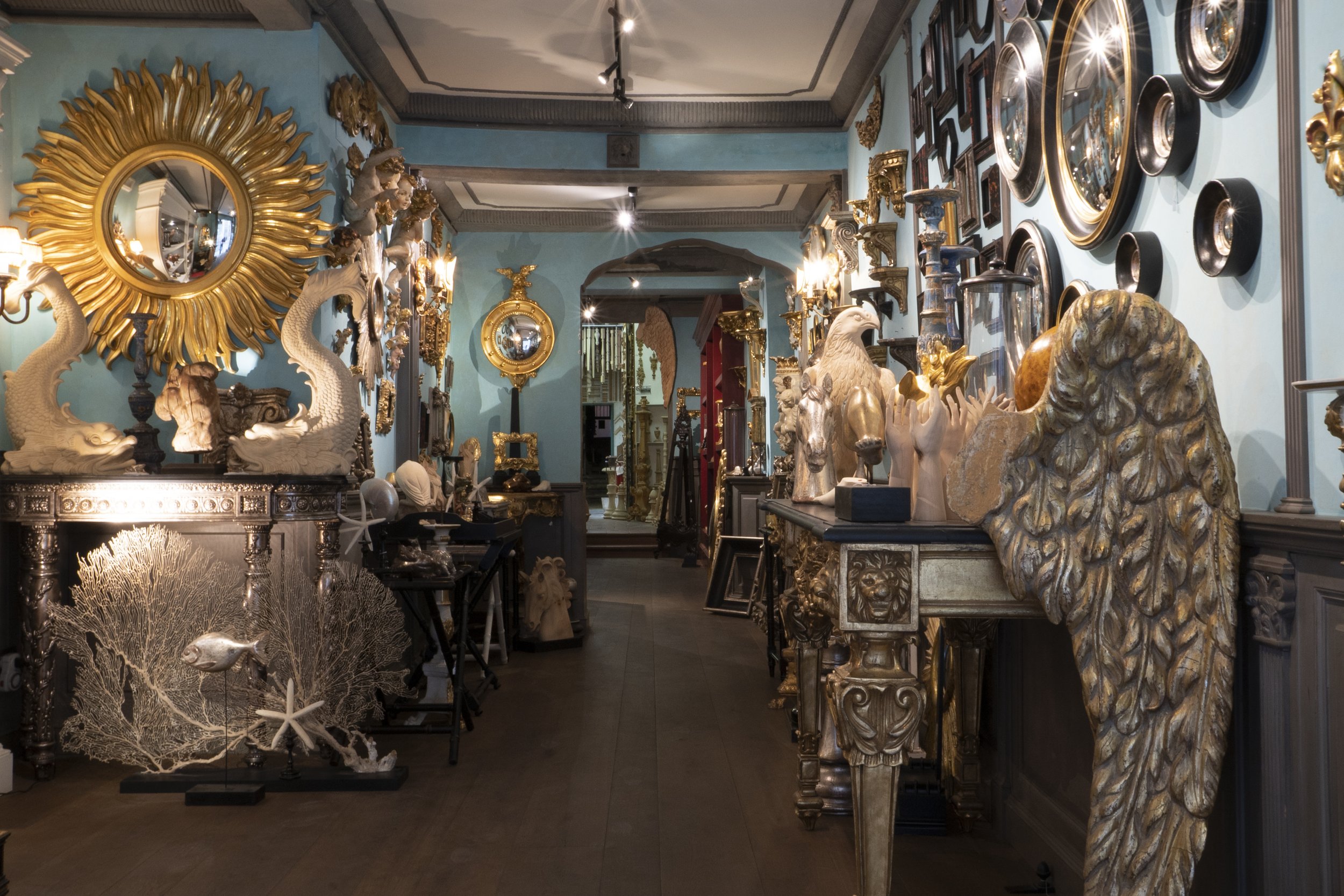 Interior of an antique shop filled with ornate gold and silver sculptures, mirrors, and picture frames on light blue walls.