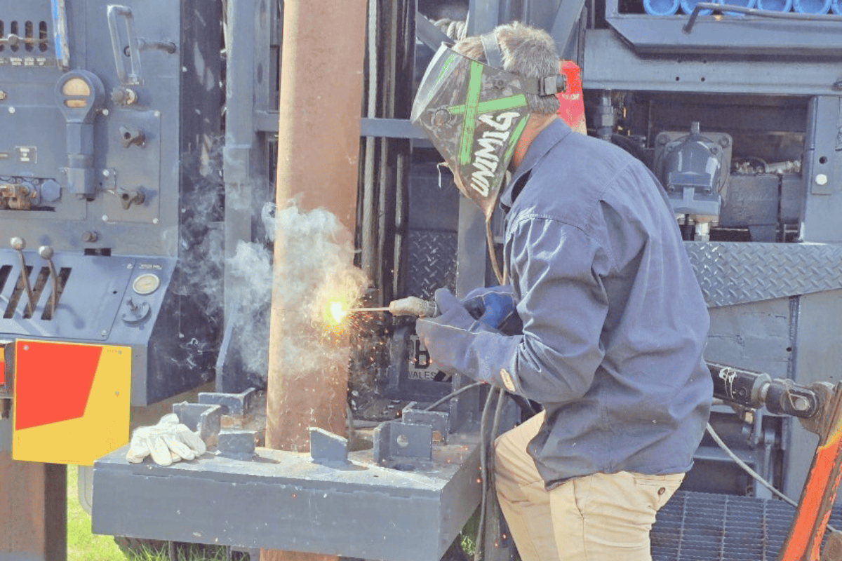A person welding metal on a construction site wearing protective gear, including a welding helmet and gloves.