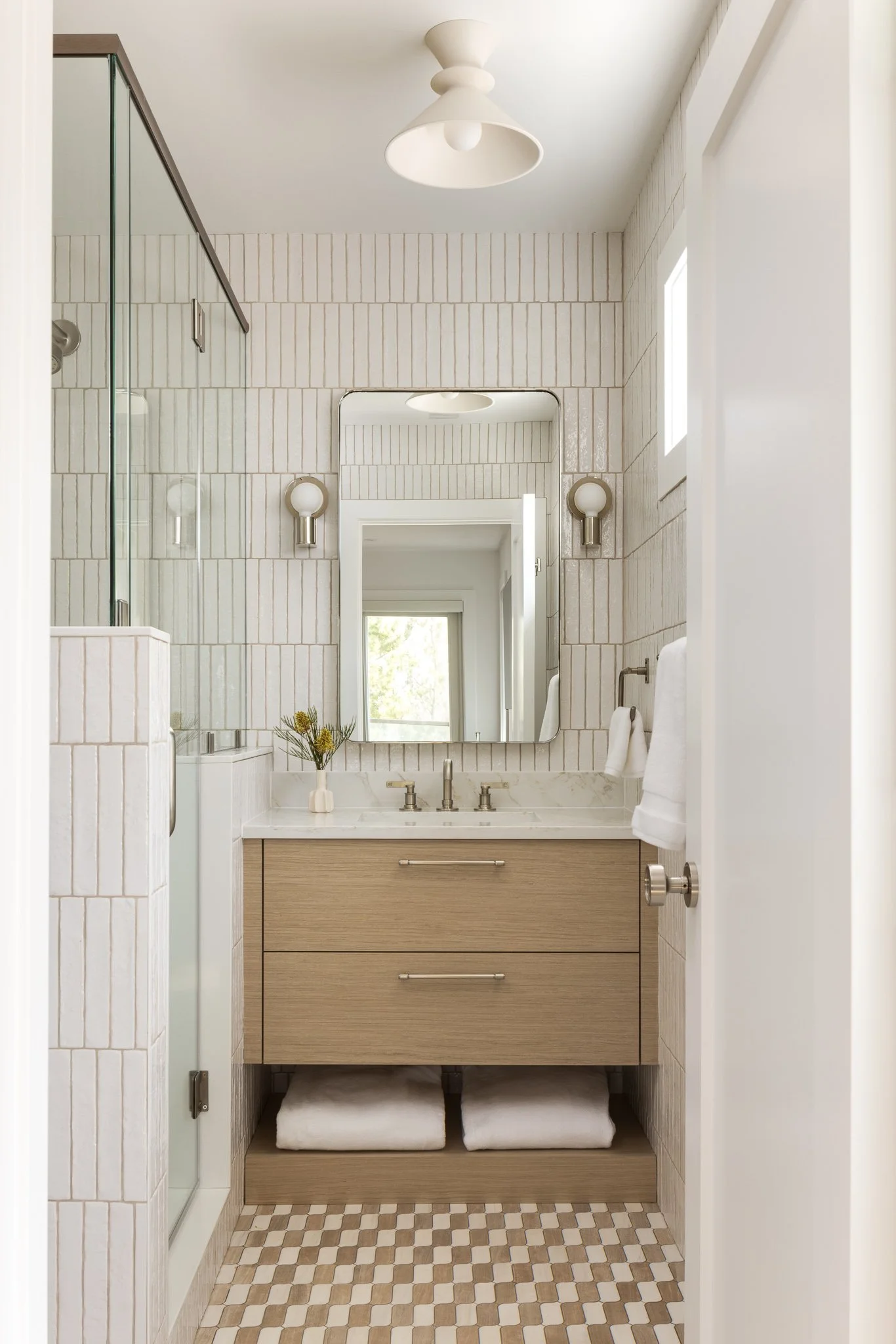 white tiled bathroom with a marble and light wood vanity and squiggly floor tiles