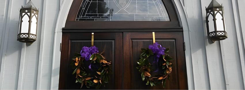 Double wooden door with two purple and brown floral wreaths hanging on each side, flanked by two lantern-style light fixtures.