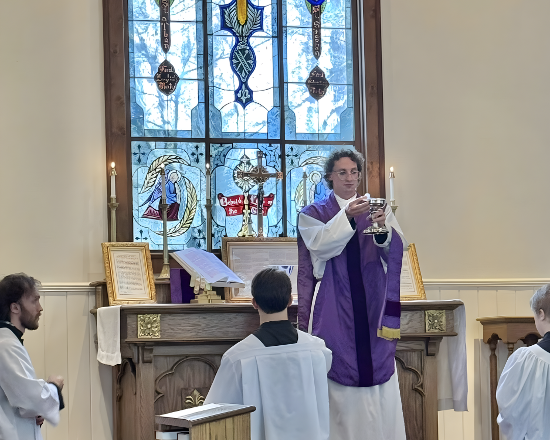 A priest in purple vestments holding a chalice during a church service, with altar and stained glass window in the background.