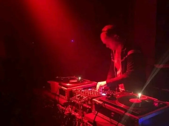 DJ performing with turntables and mixer in a dark, red-lit environment.