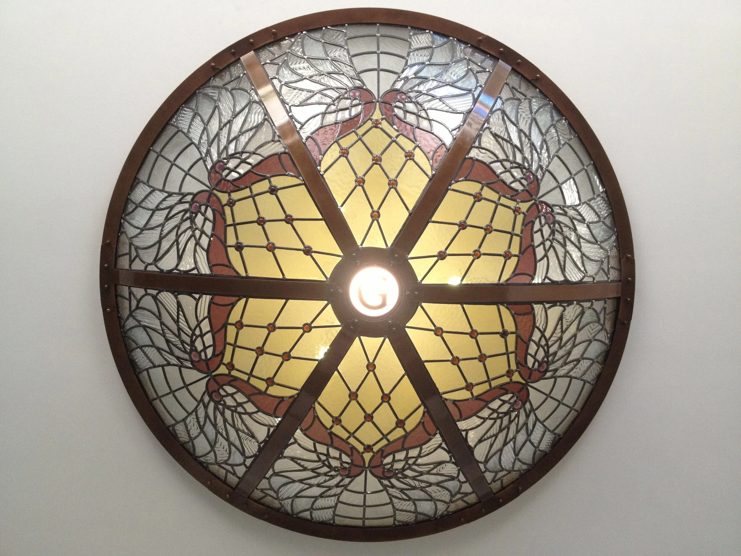 A stained glass wall art featuring a large strawberry design with intricate web-like patterns and a light fixture at the bottom center.
