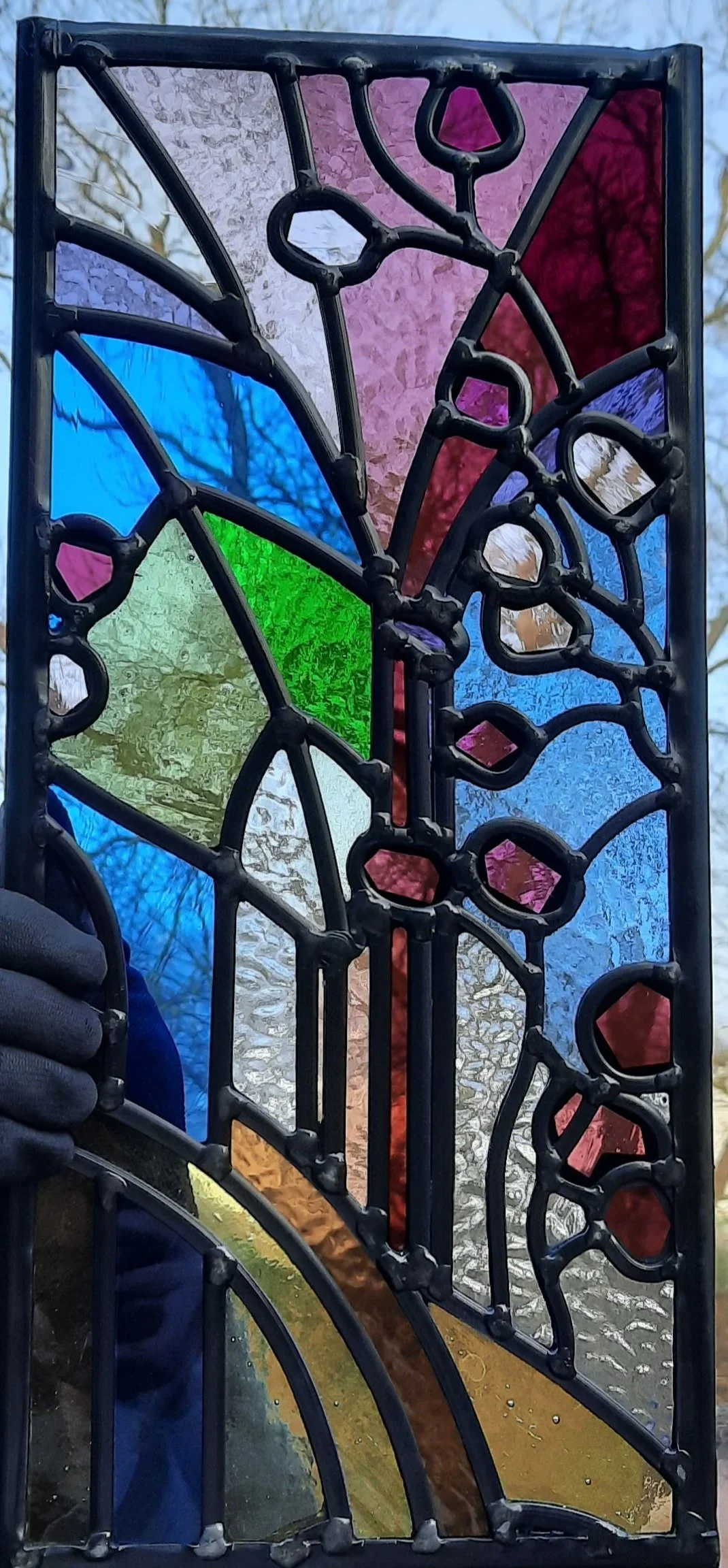 Colored glass stained glass panel with abstract patterns, including curved lines and shapes in blue, purple, red, green, and yellow, set in a black metal frame.