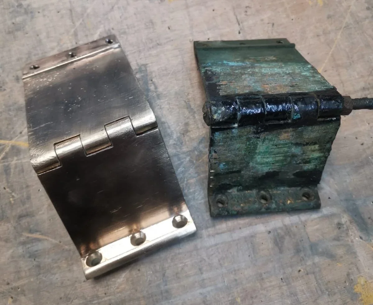 A pair of metal door hinges, one new and shiny, the other old and corroded.