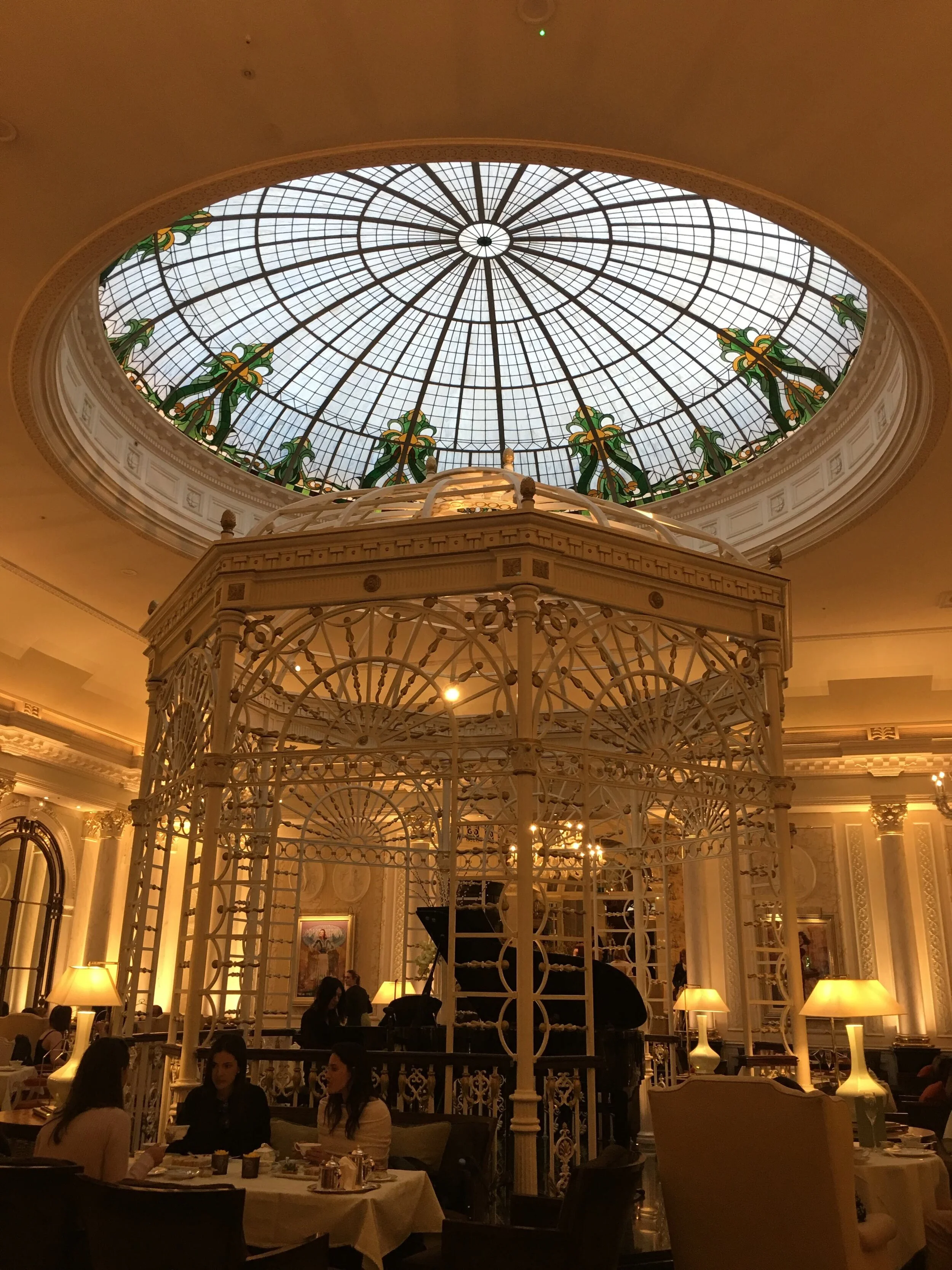 Elegant restaurant with a large stained glass dome ceiling, ornate white iron gazebo, and tables set with people dining.