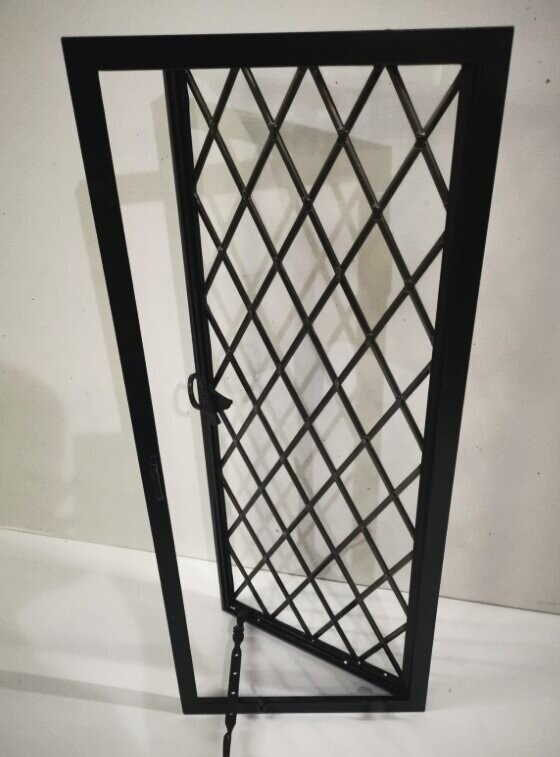 A black metal security door with a diamond lattice pattern leaning against a white wall.