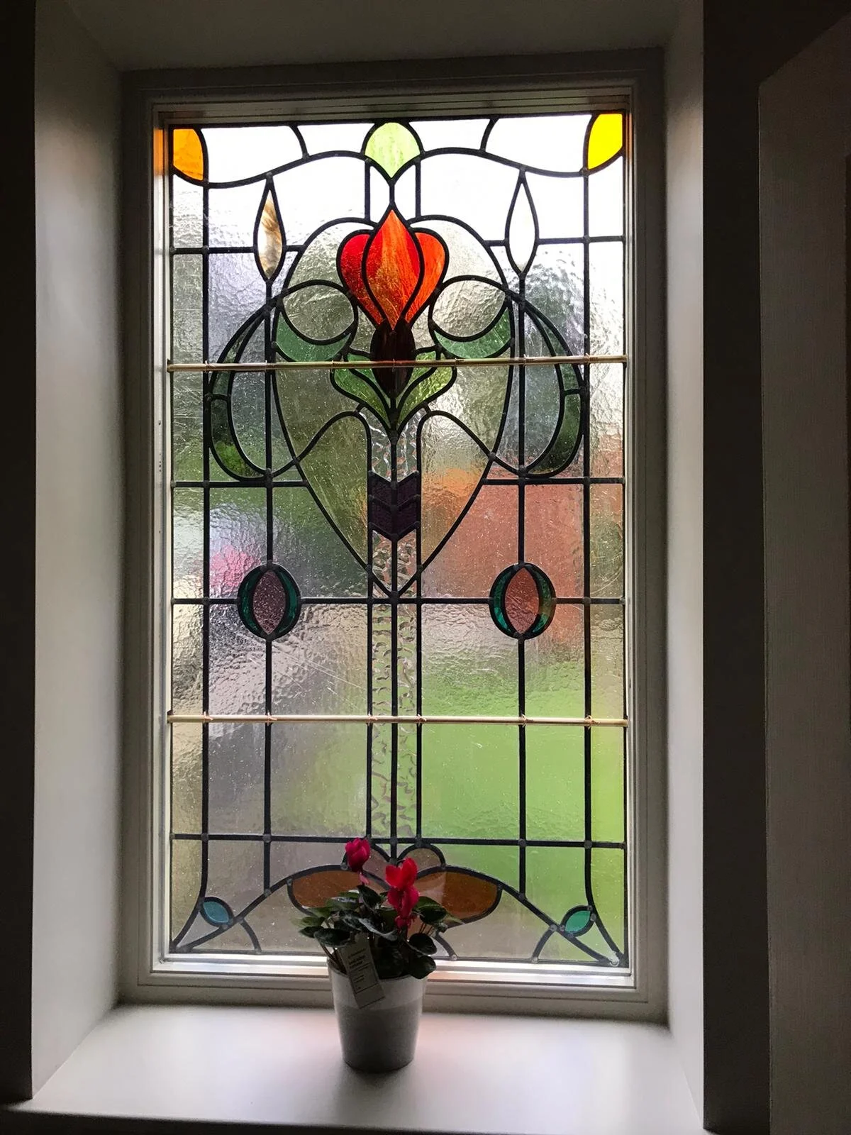 Decorative stained glass window with a potted plant with pink flowers on the window sill.