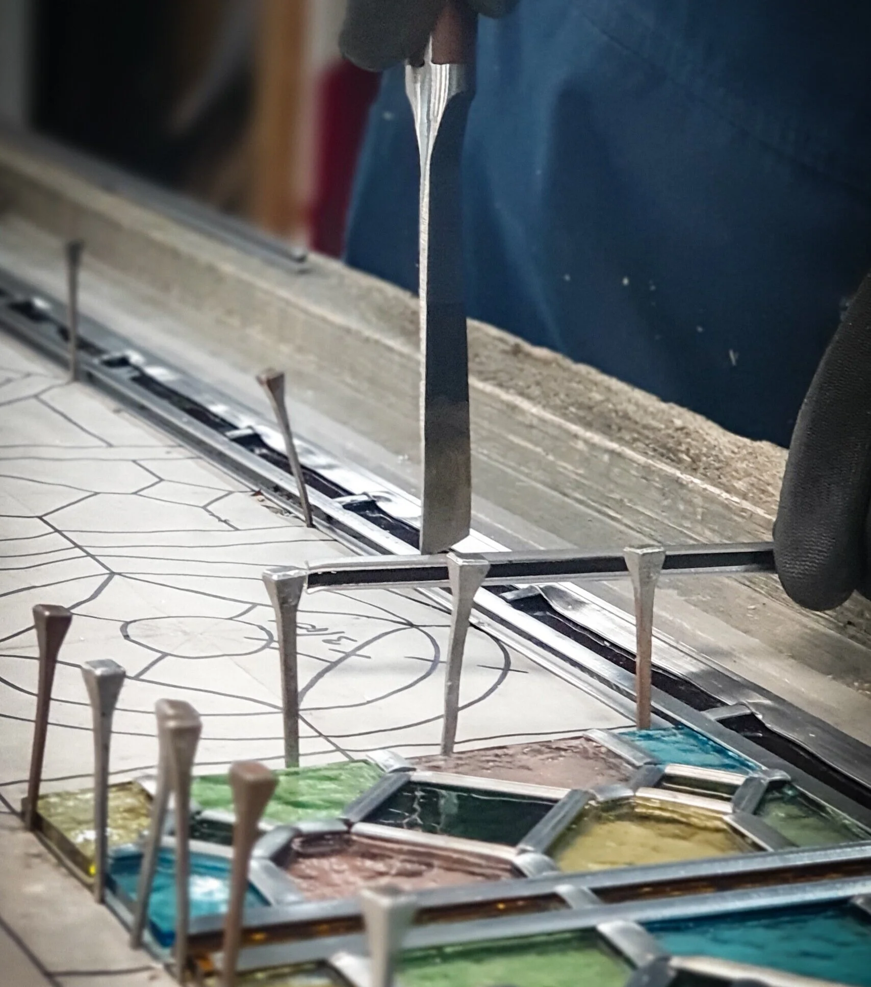 Glass palette with colorful gel paints and spatula tool being used for painting or glasswork.