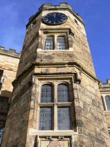 A stone clock tower with a large round clock face at the top, set against a clear blue sky.