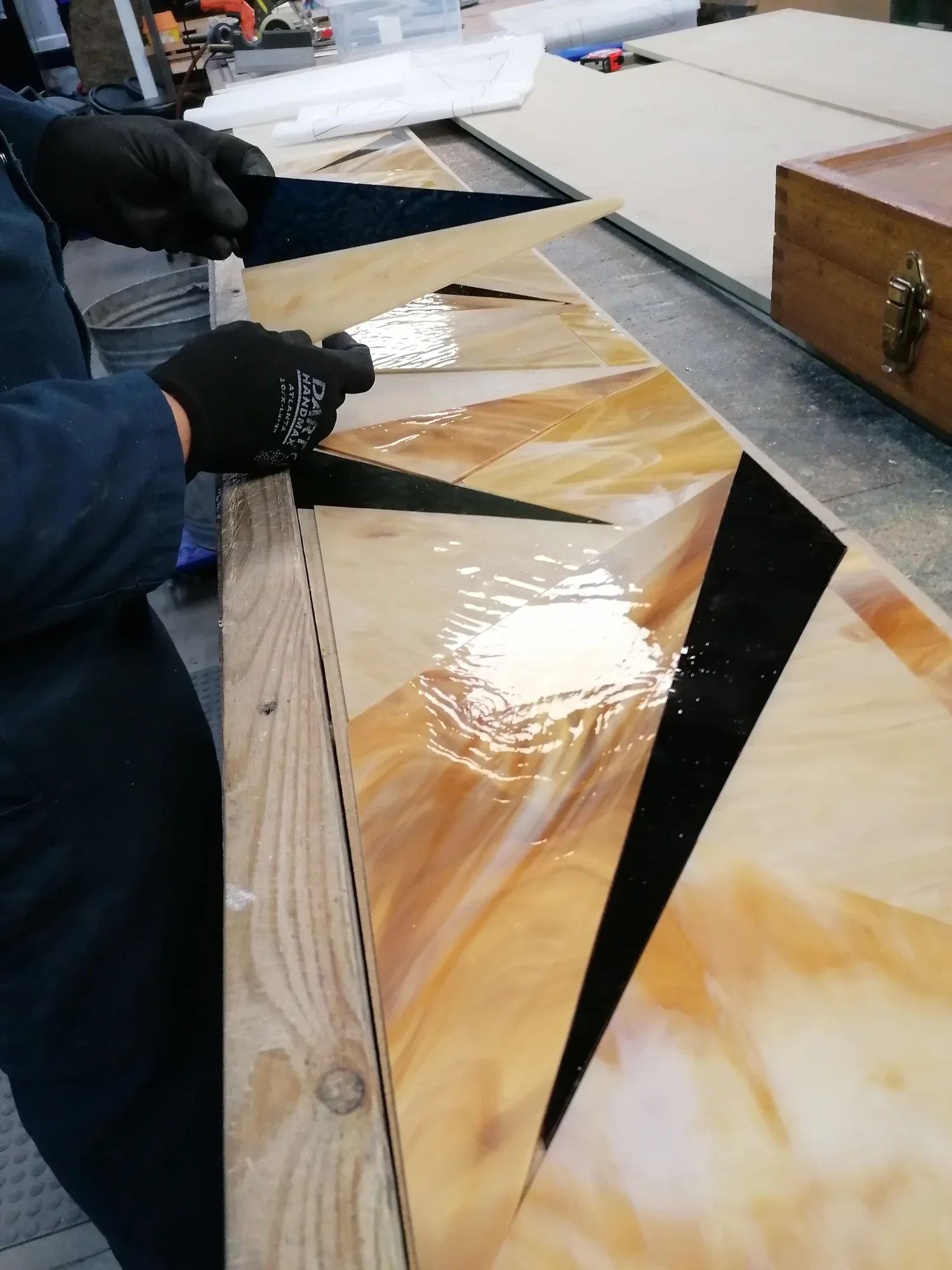 Person working with a large, glossy, geometric patterned onyx or marble slab, wearing black gloves and a blue jacket, in a workshop setting.