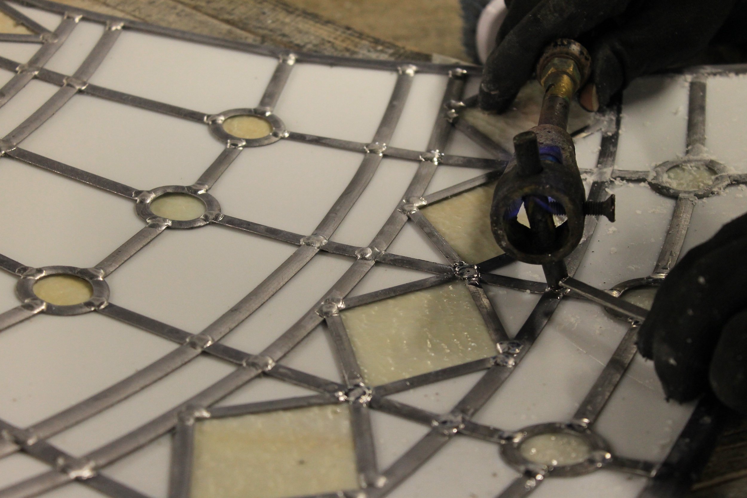 A person welding a decorative metal grating with geometric patterns onto a surface.