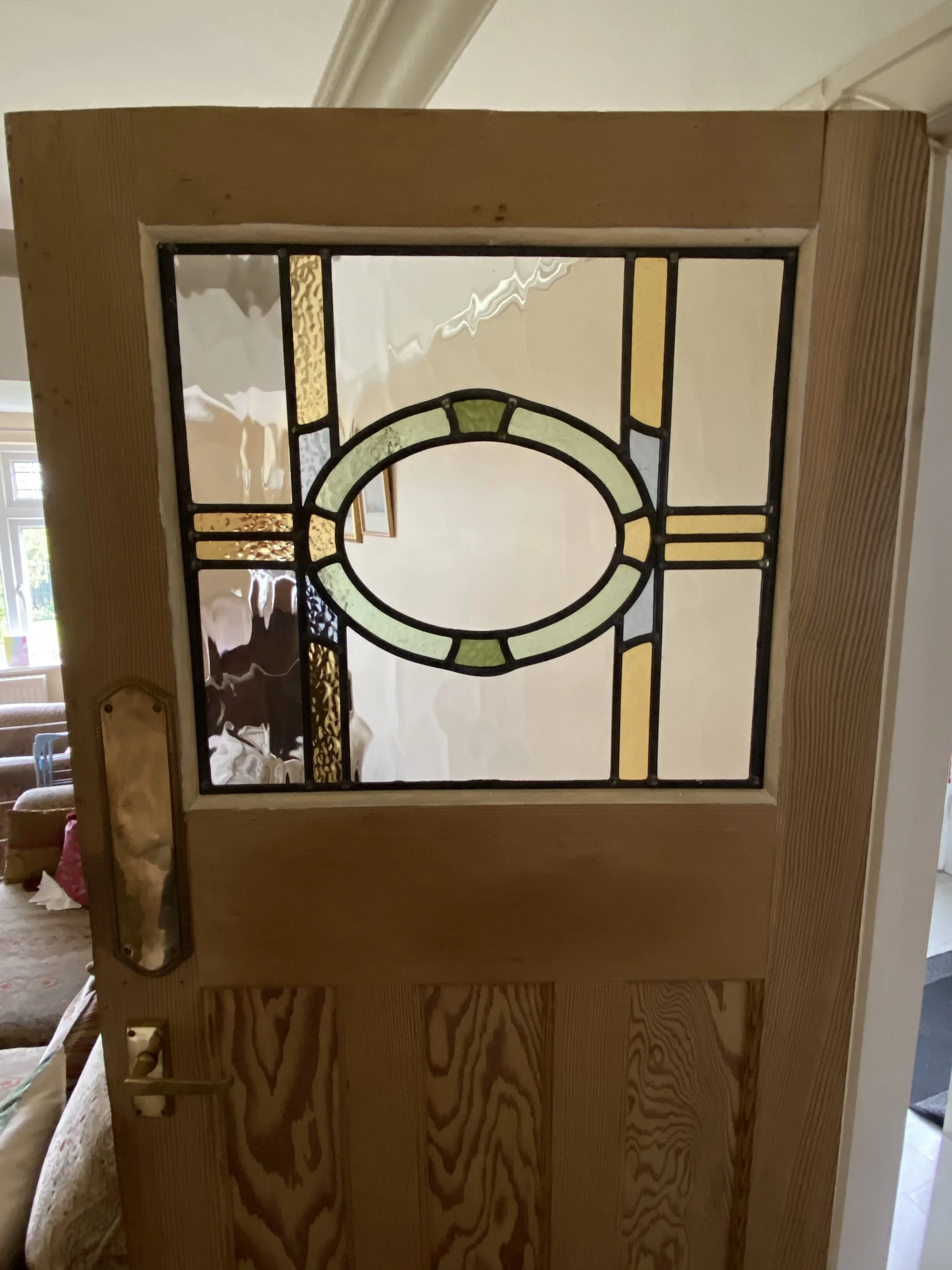 A wooden frame with stained glass panels being assembled or installed indoors, with a beige wall and window in the background.