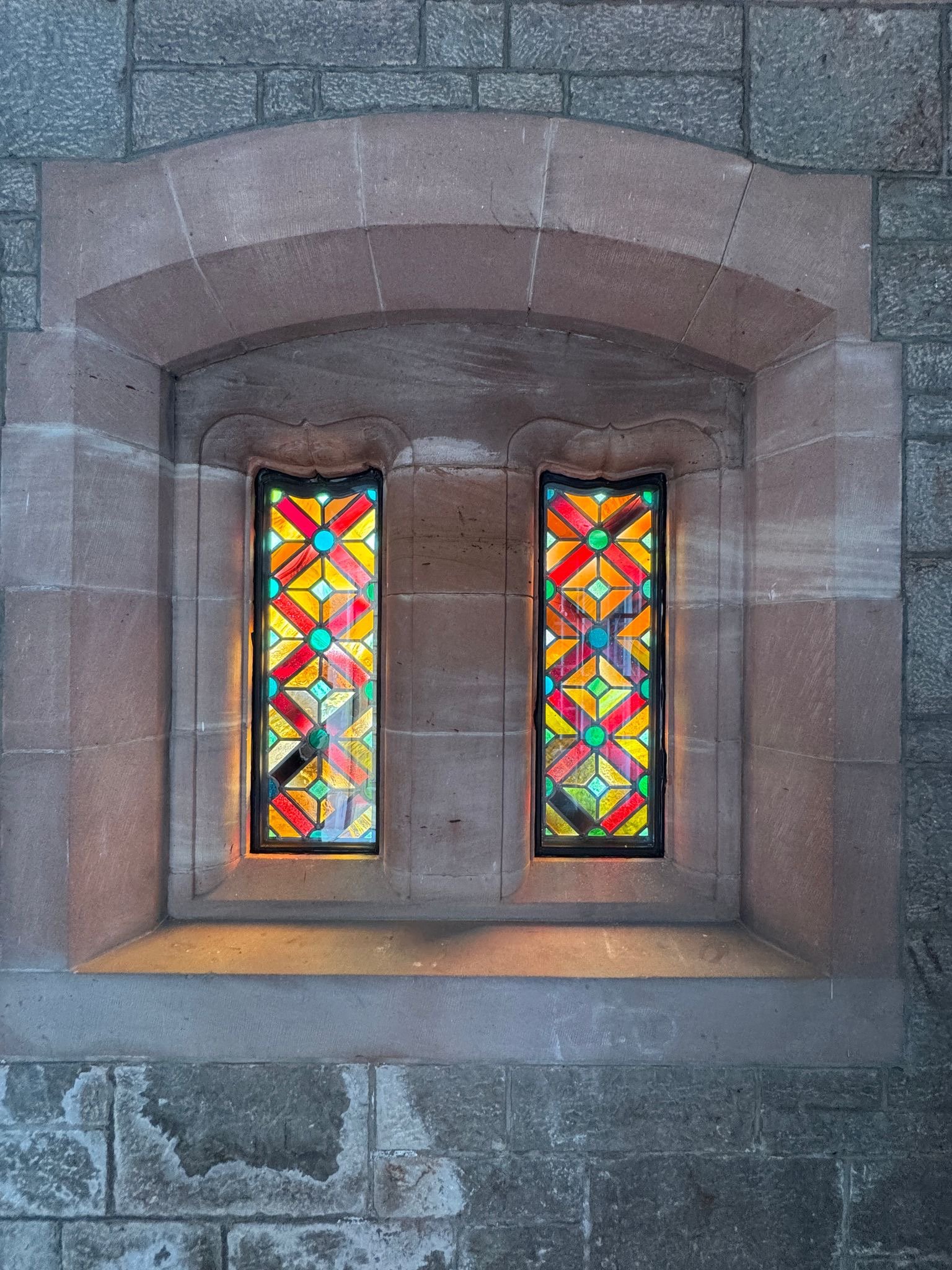 A stone wall with a colorful stained glass window featuring geometric patterns.