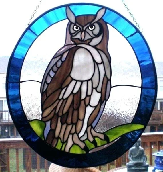 Colorful stained glass window depicting a detailed owl perched on a branch, with a circular blue border.