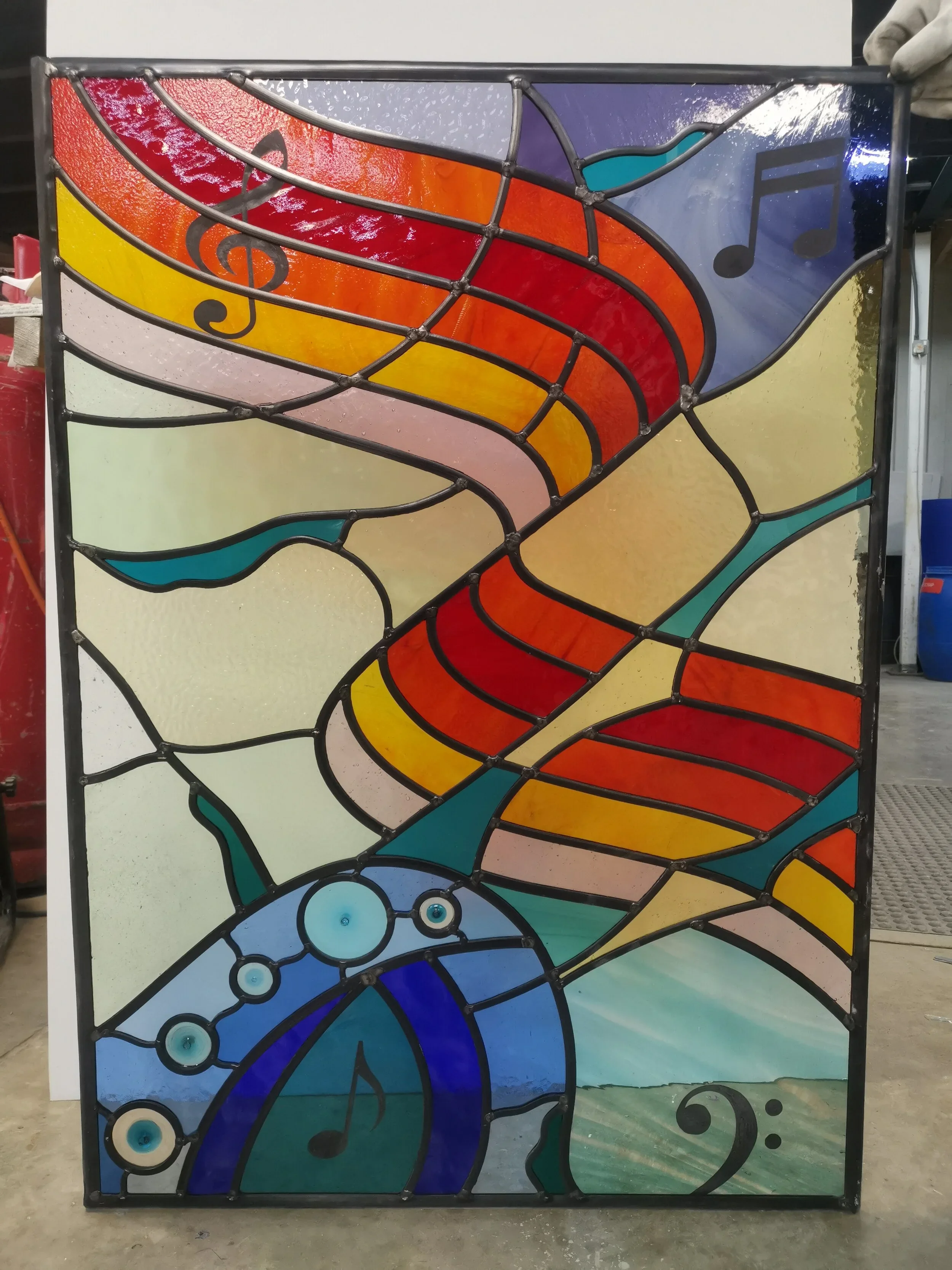 A colorful stained glass artwork featuring abstract musical notes and swirling patterns in shades of red, yellow, blue, green, and purple.