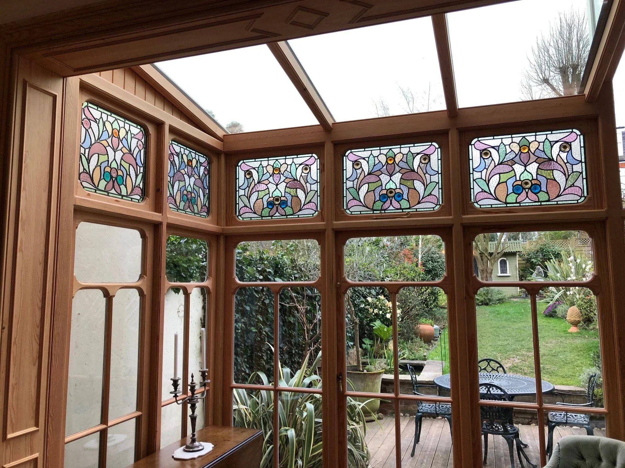 A sunroom with stained glass windows, a glass ceiling, and view of a garden with patio furniture.