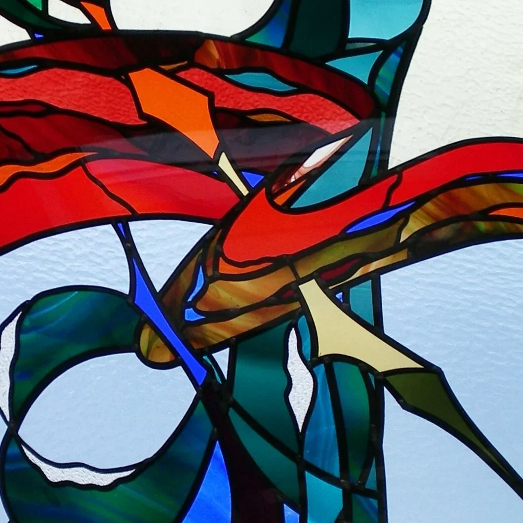 Close-up of a colorful stained glass art depicting a bird with red, orange, and blue feathers, and green leaves.