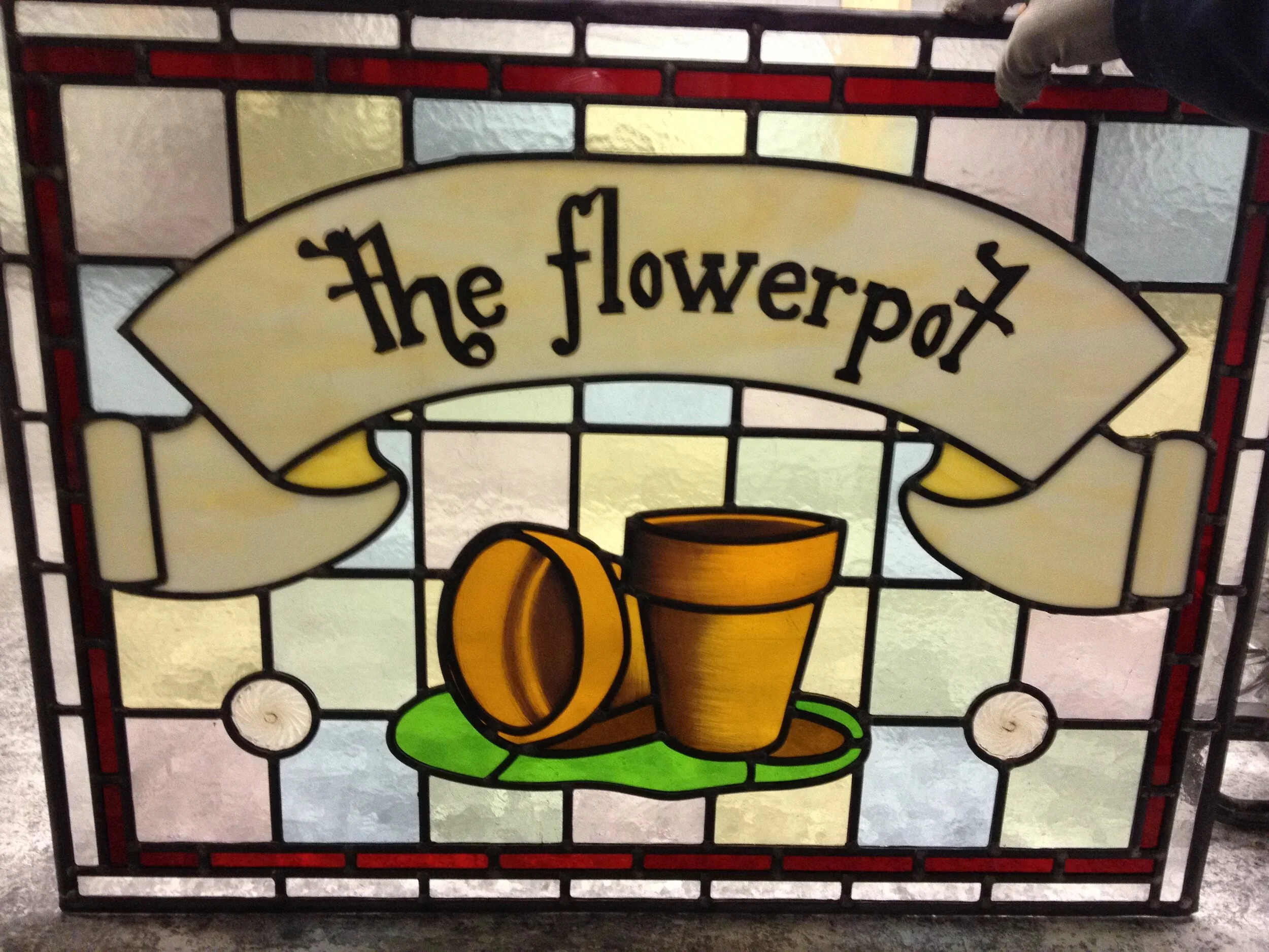 A stained glass style sign with the words 'the flowerpot' and images of flowerpots and other decorative elements.