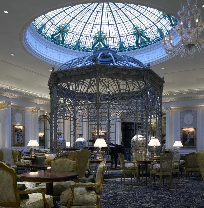 Elegant hotel lobby with a glass-domed ceiling, ornate chandelier, large decorative birdcage, and comfortable seating.