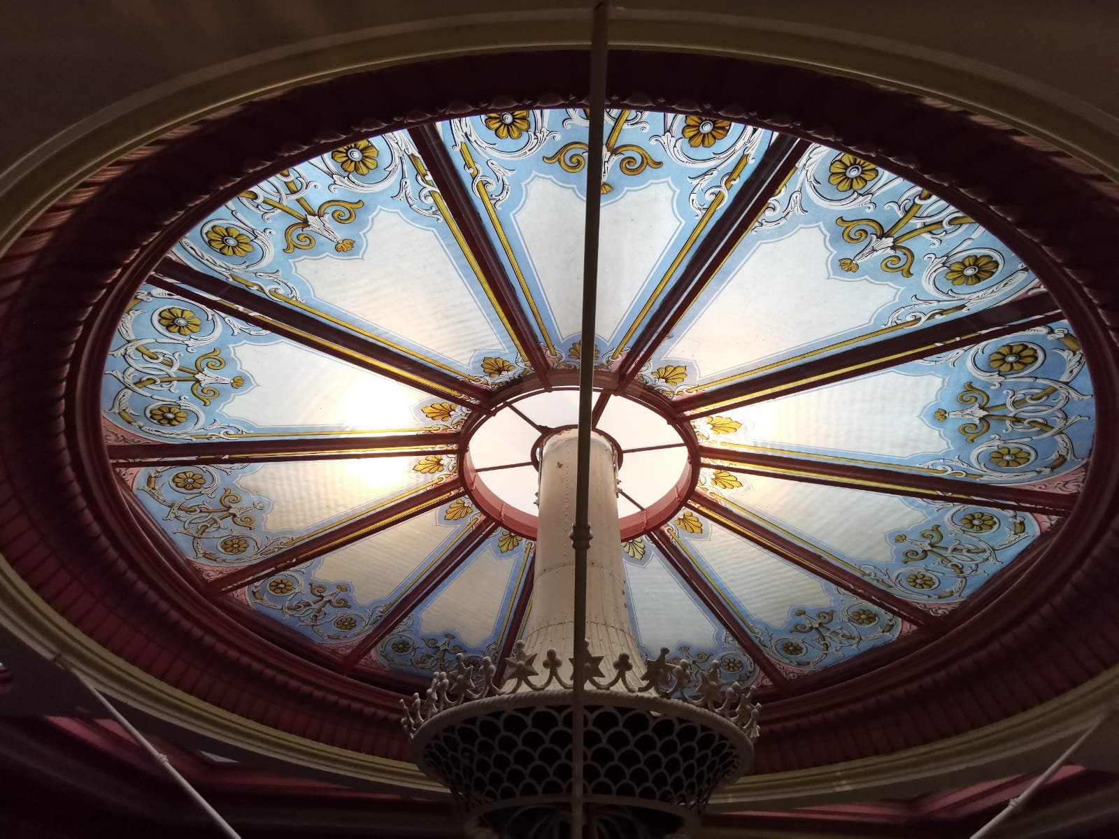 Close-up view of a decorative, stained glass ceiling with floral and geometric patterns, seen from below.