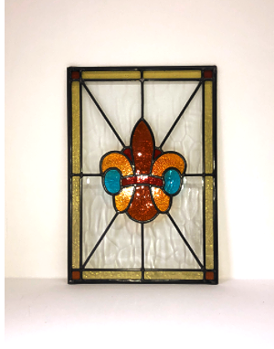 A stained glass window with a fleur-de-lis design, featuring yellow, orange, blue, and black glass pieces.