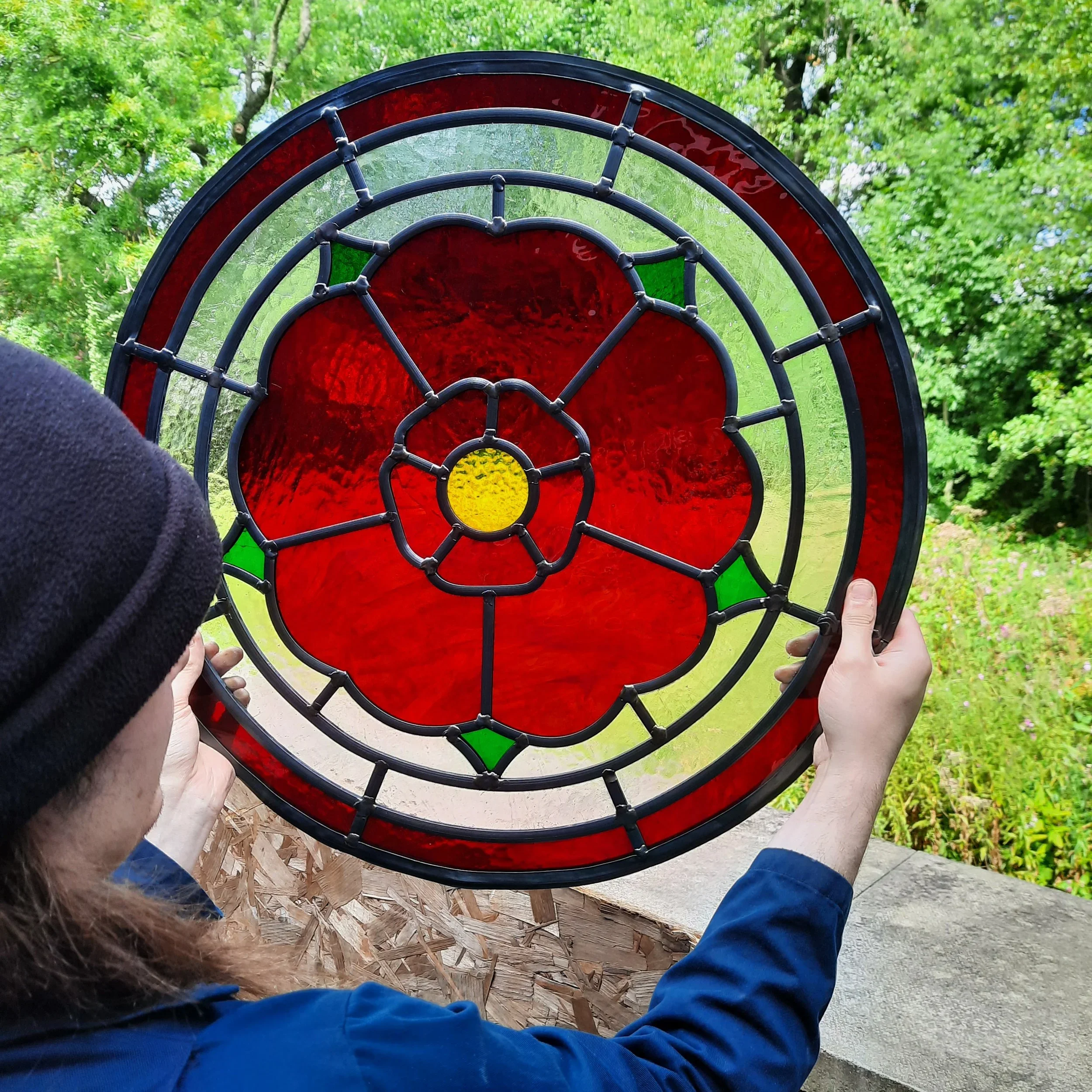 Person holding a colorful stained glass window panel outdoors, with green trees in the background.