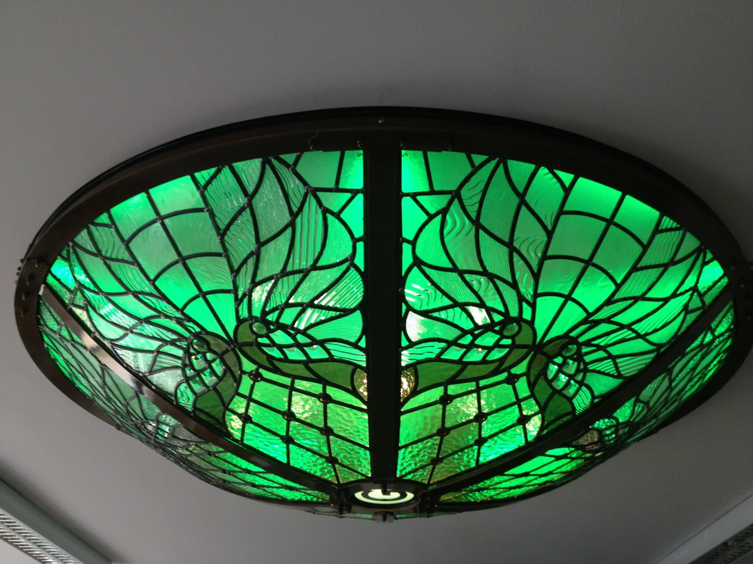 Close-up of a stained glass ceiling light fixture with green glass and black metal framework.