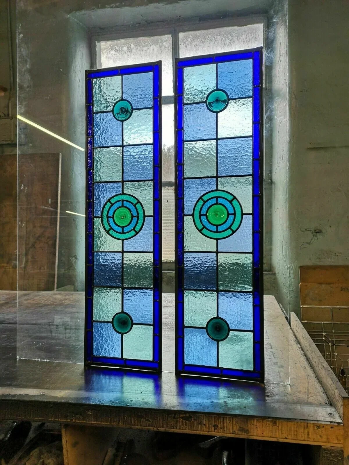 Stained glass window with blue, green, and textured glass panels in an interior setting.