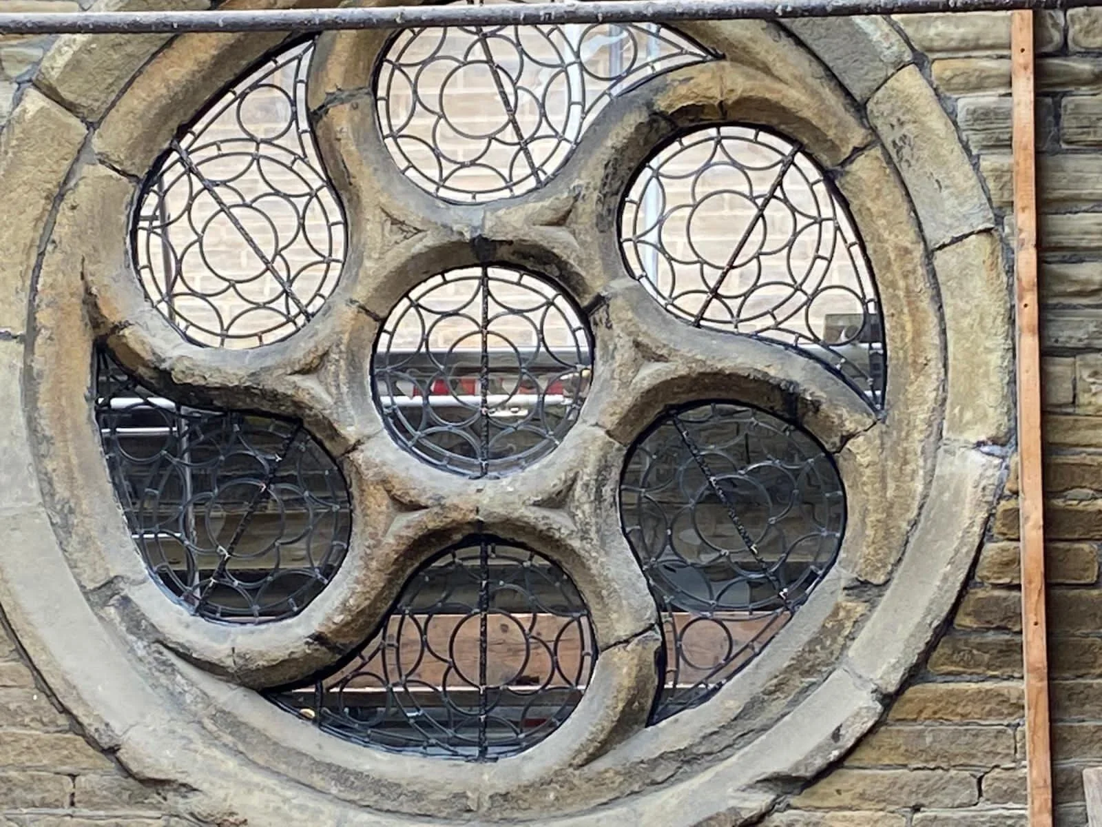 A decorative stone and metal window with a floral or geometric pattern, set into a brick wall.