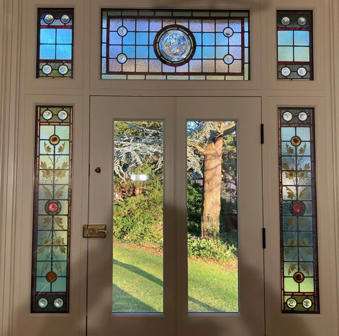 A front door with stained glass windows and a view of a backyard with trees and green grass.
