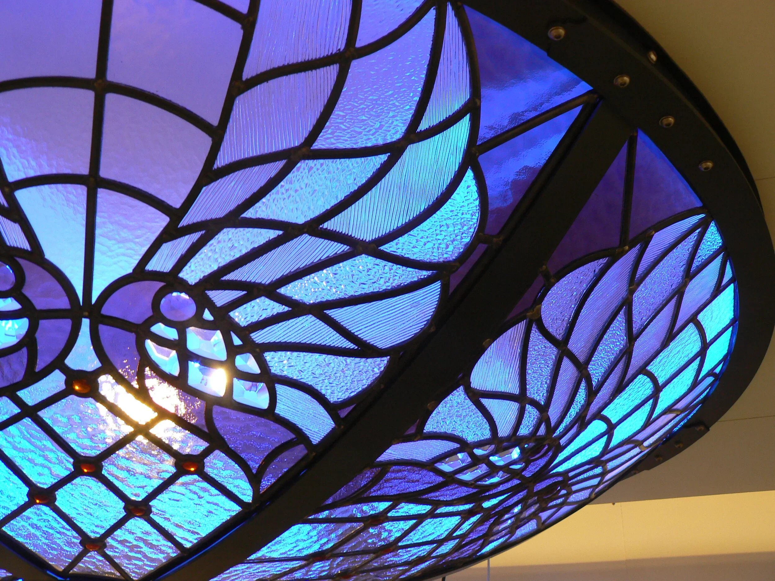 Close-up of a stained glass ceiling with blue and purple hues, featuring an intricate design with black metal framing.