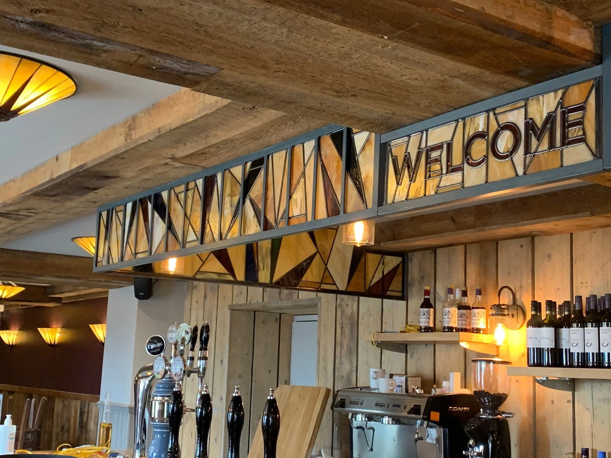 Interior of a restaurant or bar with wood accents, a bar counter with taps, and a illuminated 'WELCOME' sign on a wall.