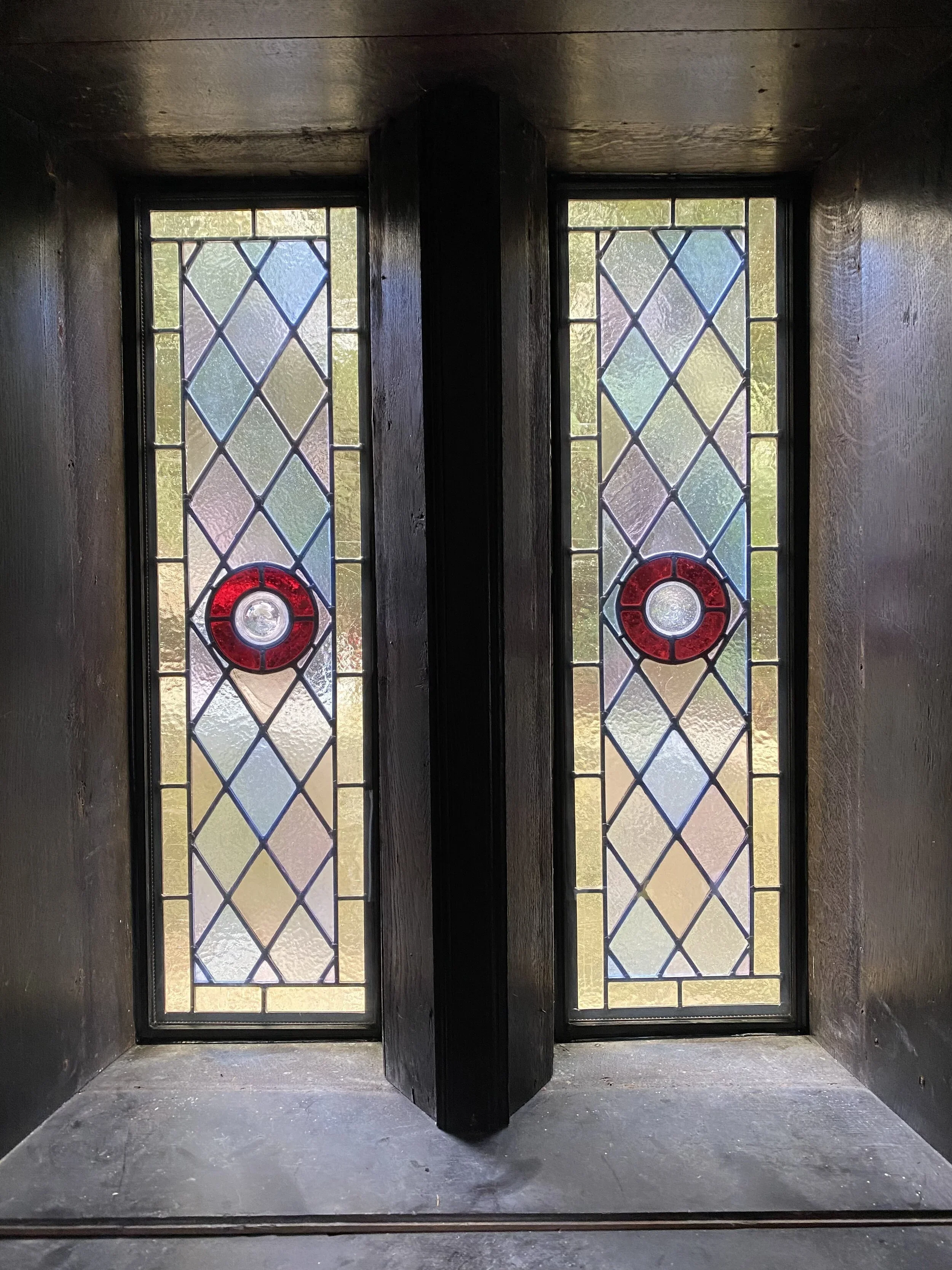 A stained glass window with diamond-shaped patterns and red circular accents in a dark, enclosed space.