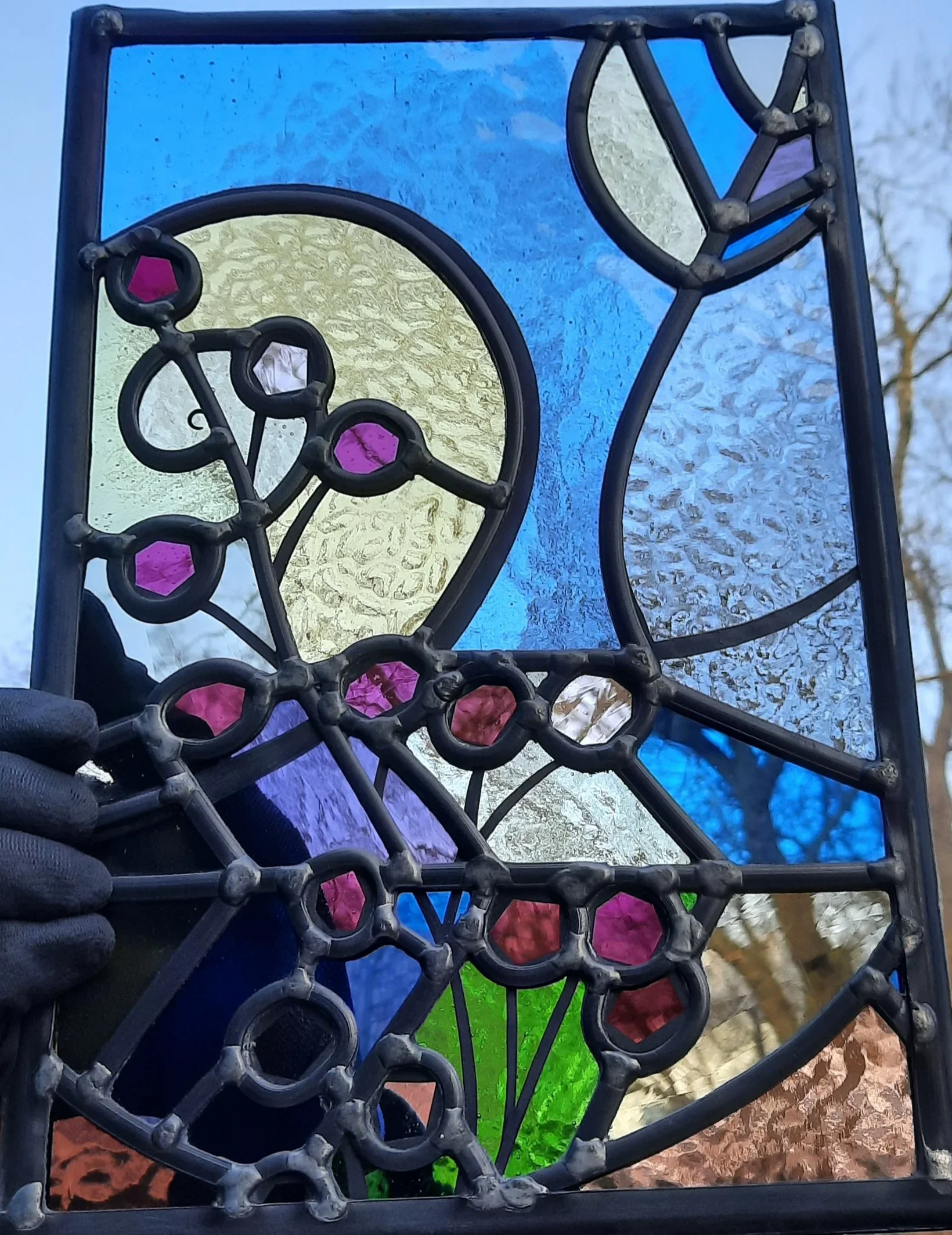 Colorful stained glass window with geometric and floral patterns, featuring shades of blue, green, yellow, pink, purple, and red.