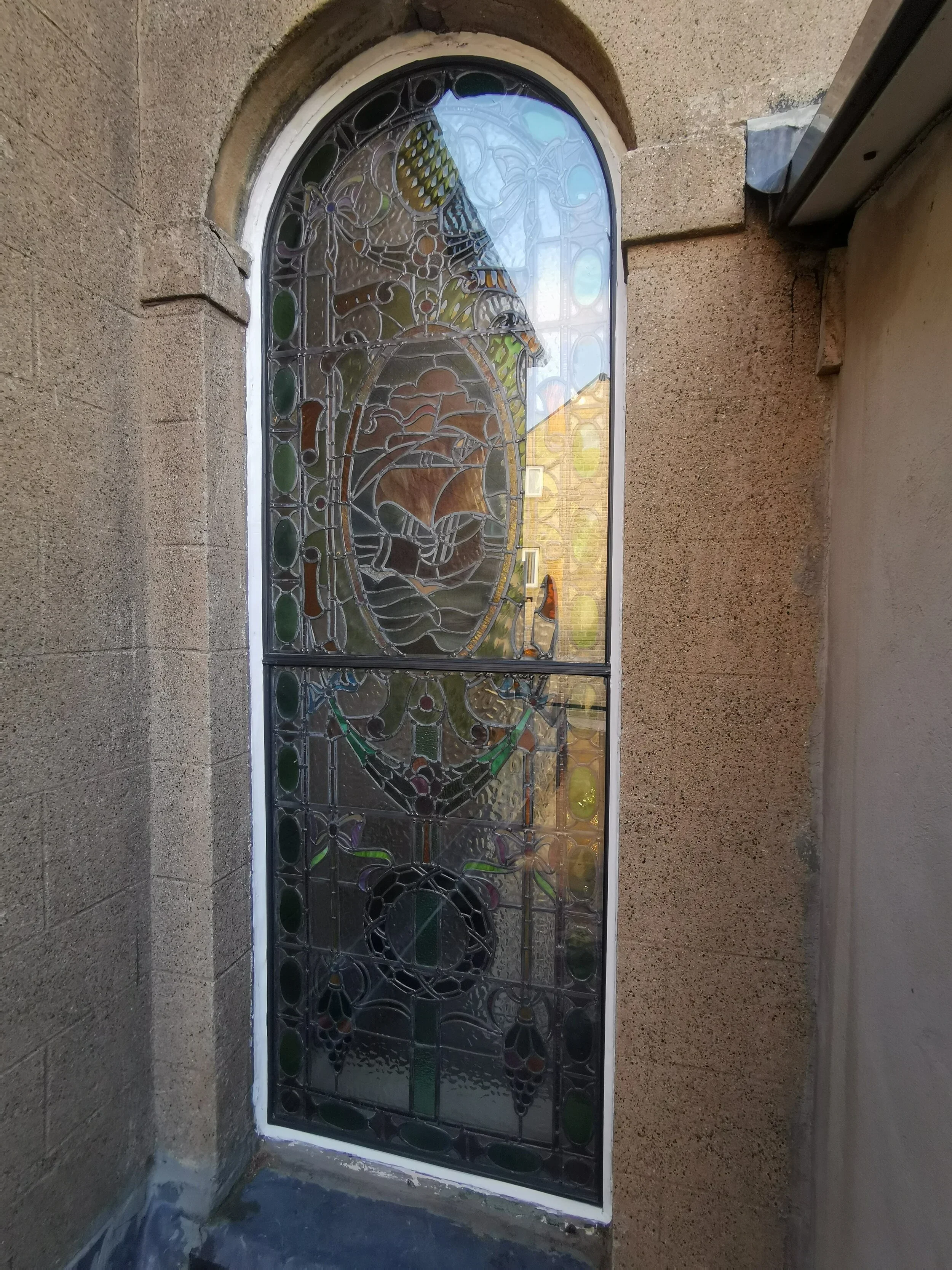 Decorative stained glass window with floral and geometric patterns set in a stone wall.