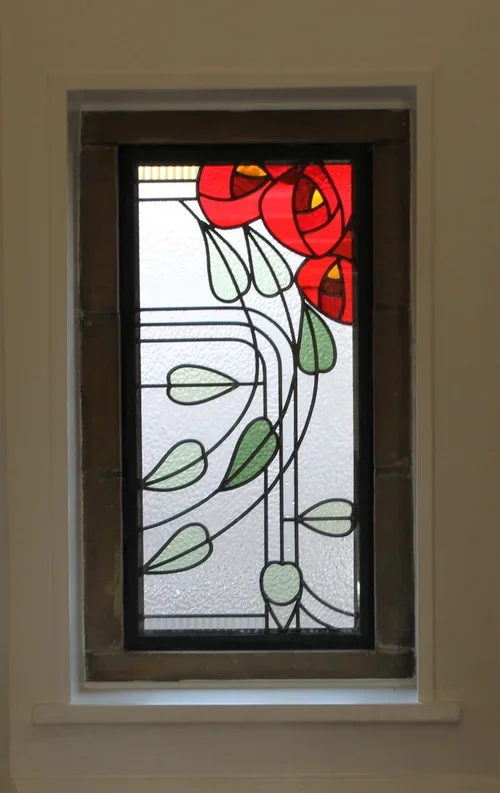 A stained glass window depicting a red rose with green leaves and black outlines.
