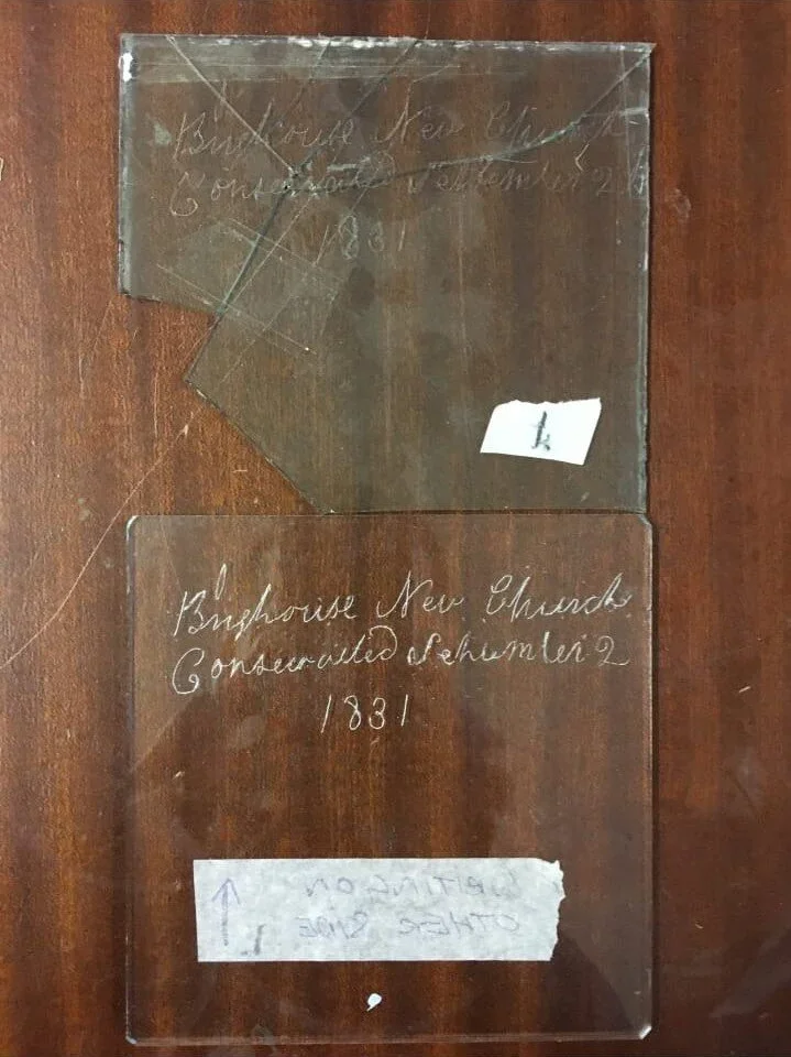 Two pieces of transparent glass with handwritten inscriptions, placed on a wooden surface. The inscriptions mention 'Bluphouse New Church Conarvalede Szenulei 2 1831' and have some tape and a sticker with the letter 'L'.