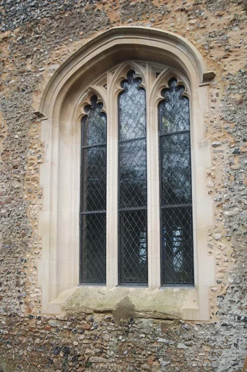 Stone wall with a Gothic-style arched window featuring stained glass and diamond-patterned leaded glass panes.