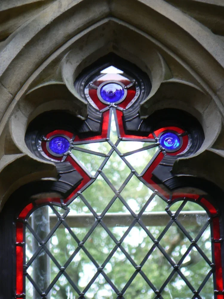 Decorative stained glass window with a star-shaped design, featuring blue circular accents and a red and clear color pattern, framed by stone architecture.