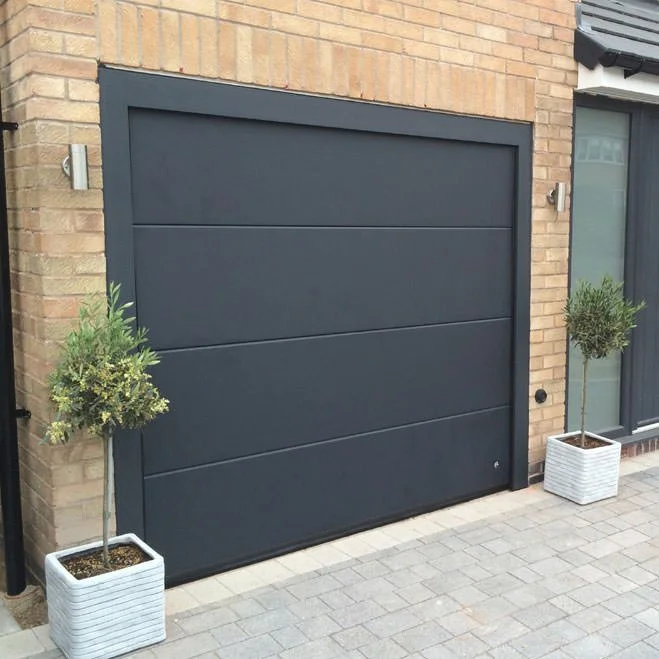 Black garage door with two potted trees on either side and brick exterior wall.
