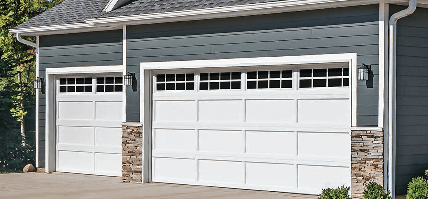 Double garage with white doors, stone accents, and exterior wall lights on a house with blue siding.