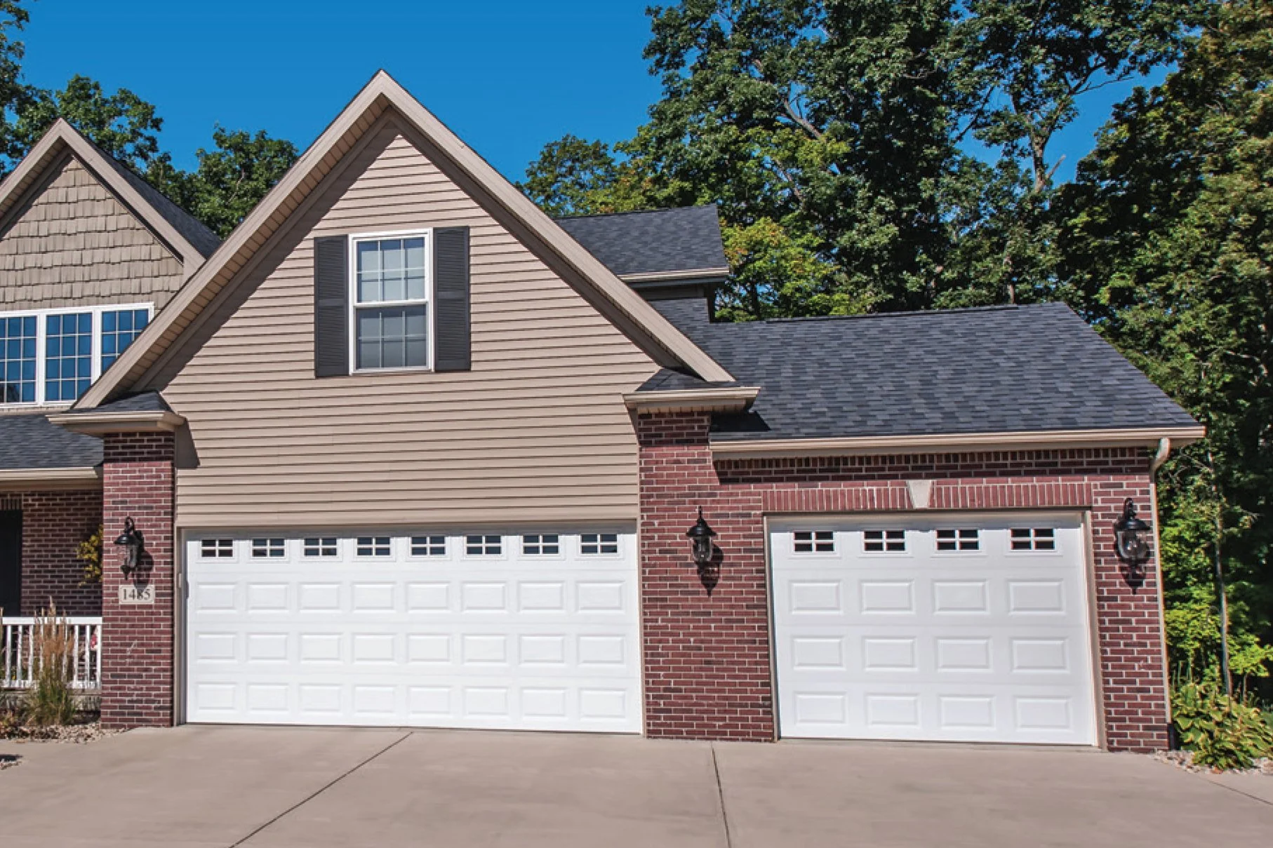 Two White Steel Traditional Raised Panel Garage Door on Brown and Brick House
