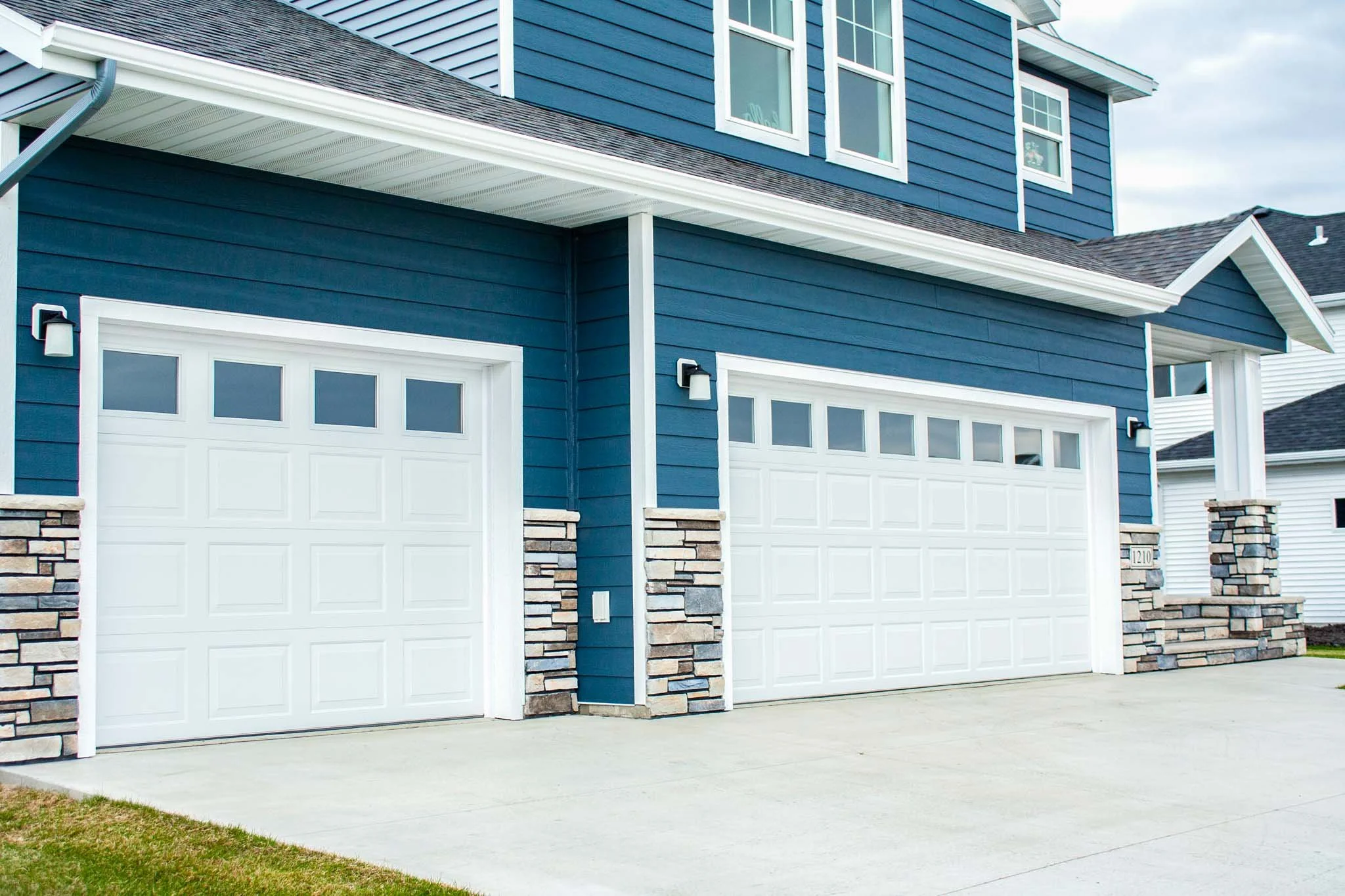 Two White Steel Traditional Raised Panel Garage Door on Blue House