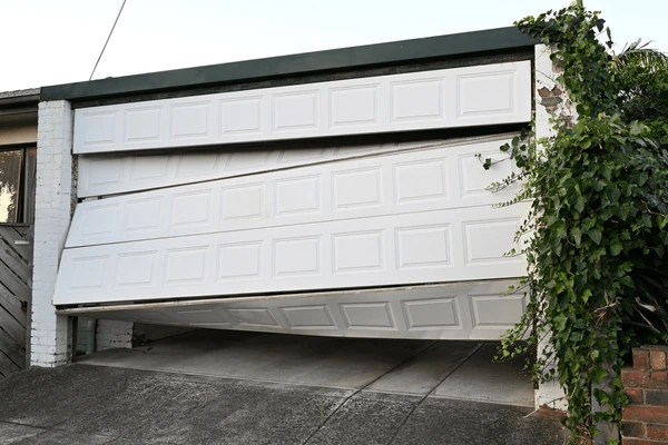 A white garage door partially open, attached to a brick building with greenery on the side.