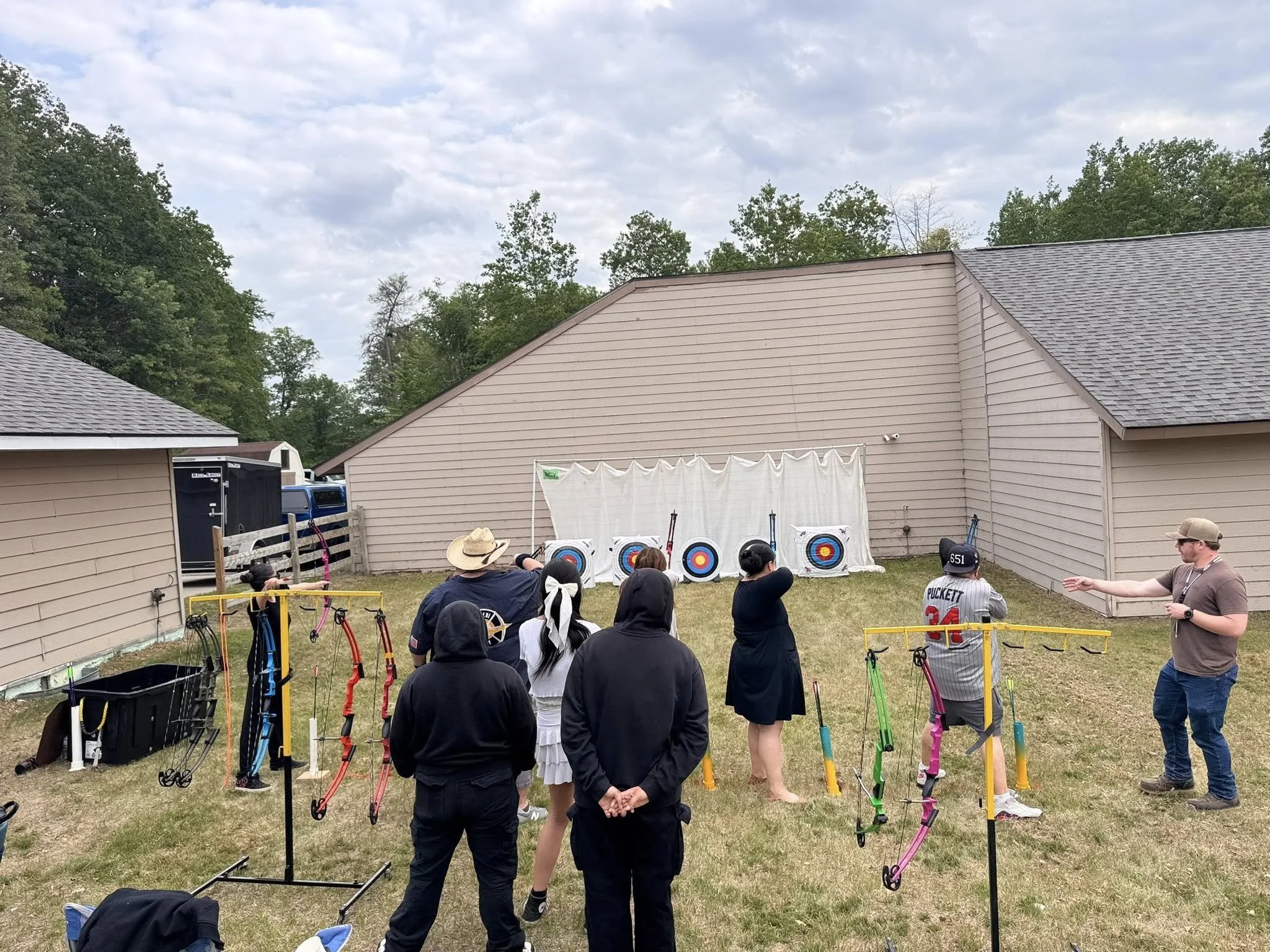 People participating in an archery practice in a backyard with targets and bows, supervising and instructing.