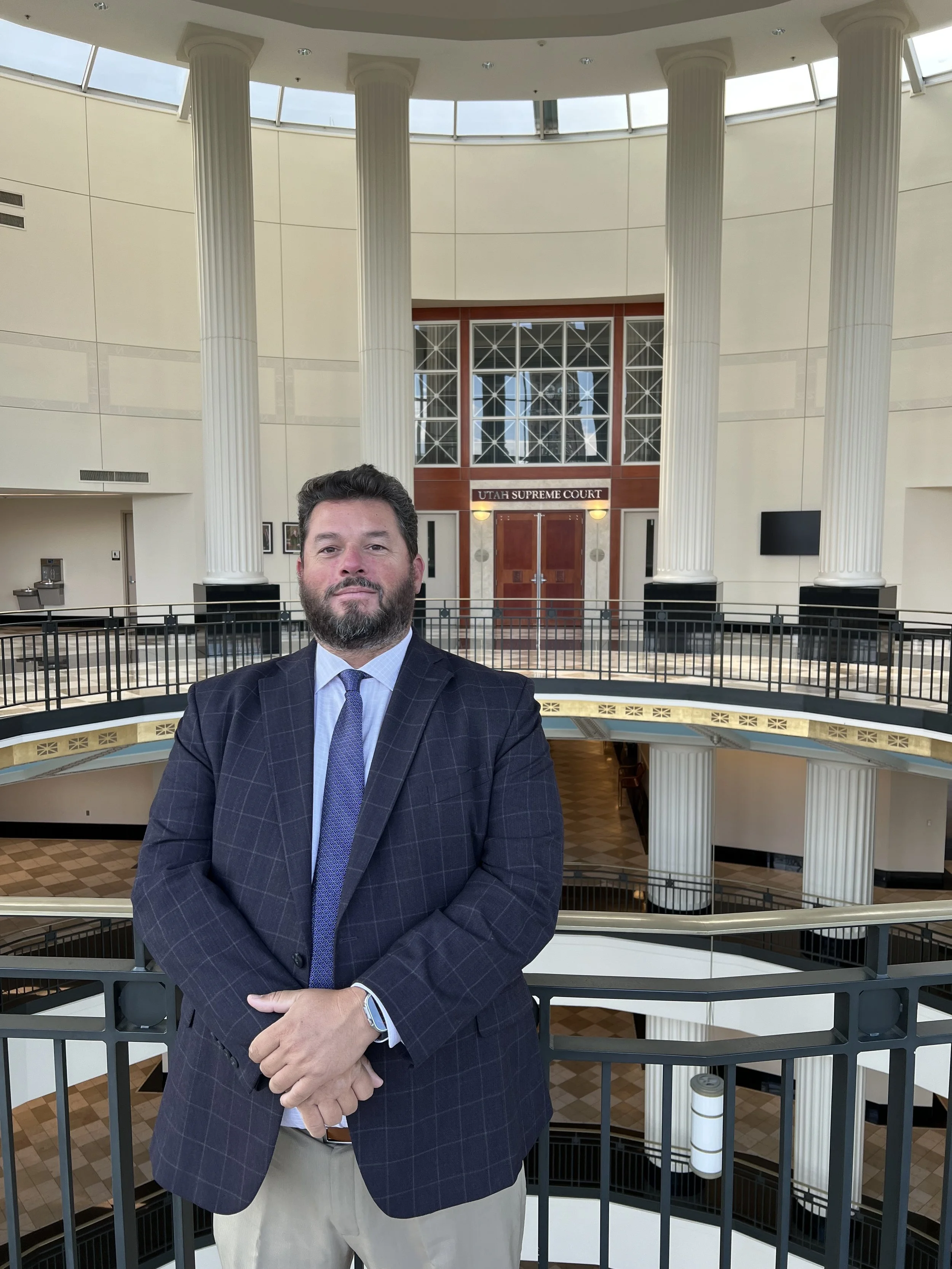 A man in a dark checkered suit and light blue shirt stands in front of Utah Supreme Court inside a courthouse.