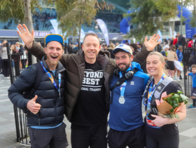 A person dressed in outdoor gear, standing on a grassy hill and looking at snow-capped mountains under a clear blue sky.